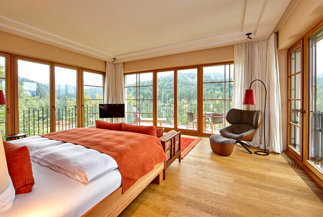 Hotel room in Schloss Elmau with bed and armchair and a clear view of the woods